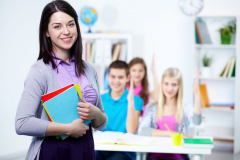 Happy teacher looking at camera with her students on background